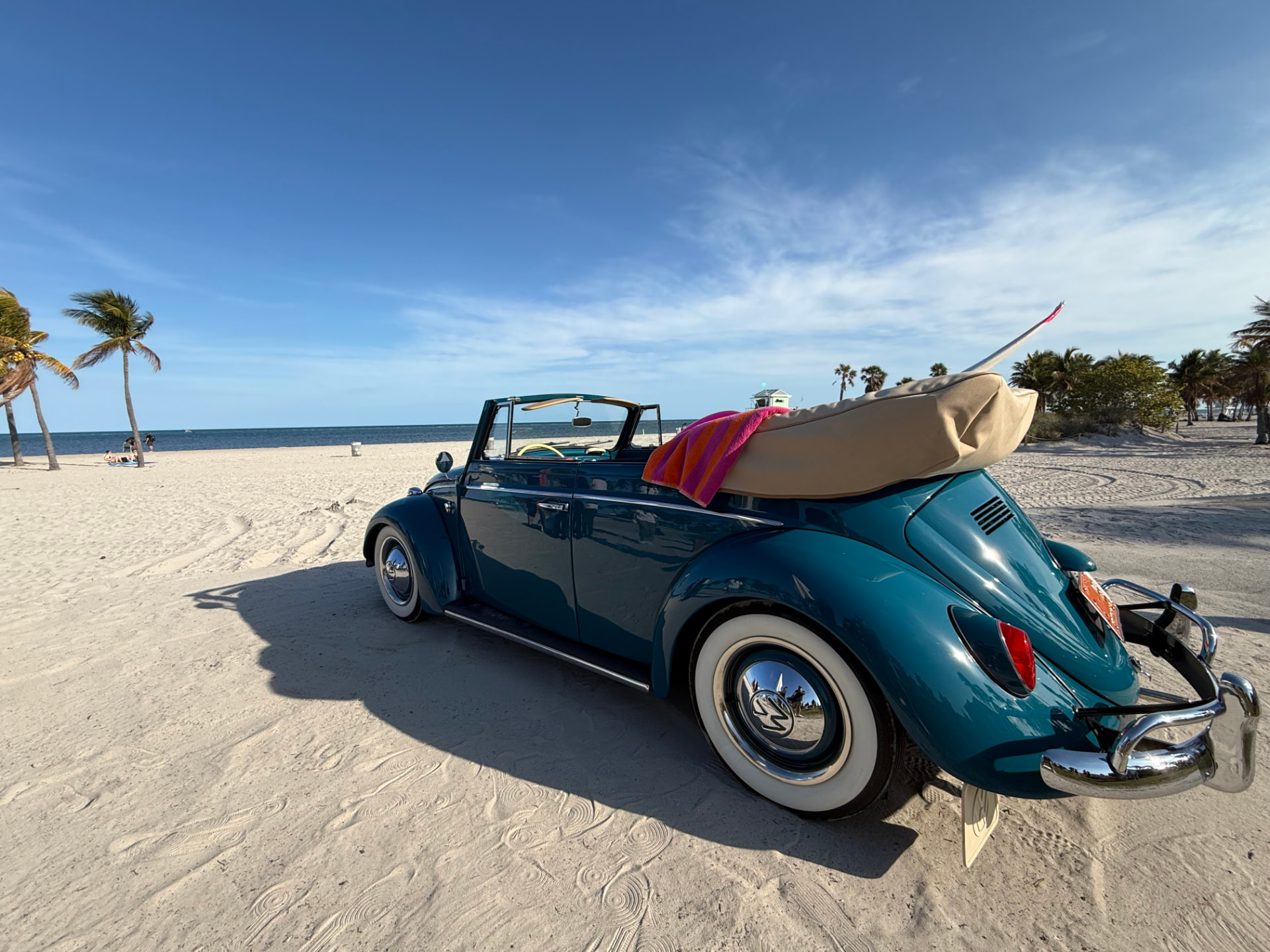 Classic teal Volkswagen Beetle convertible parked on a sunny beach with palm trees